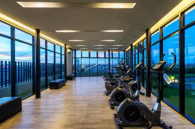 a gym with cardio equipment in a building with windows at De Botan Srinakarin Hotel & Residence in Bangkok