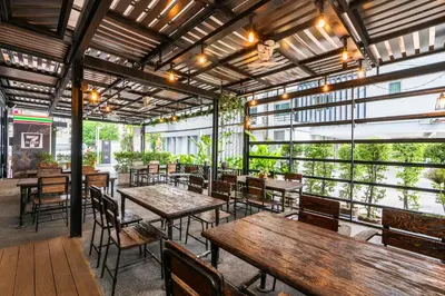 a restaurant with wooden tables and chairs and windows at De Botan Srinakarin Hotel & Residence in Bangkok