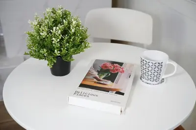 a table with a book and a cup and a plant at Deluxe Gam-Hom Hostel เจริญนคร in Bangkok