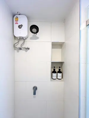 a white bathroom with a shower with two bottles of alcohol at Komfort Duplex BTS Ratchayothin in Bangkok