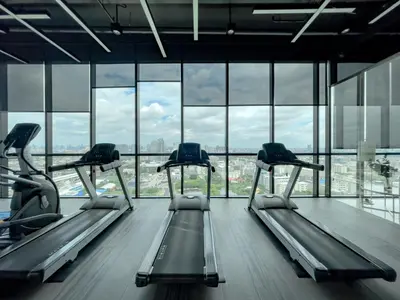 a gym with three treadmills in a room with windows at Near BTS Bearing l Rooftop pool and gym in Bangkok