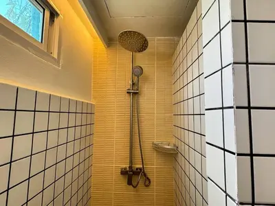 a shower in a bathroom with yellow and white tiles at Nana Best Hostel in Makkasan