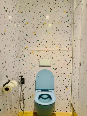 a bathroom with a toilet with confetti on the wall at Easy Monday Pool Capsule Hotel - Old Town Bangkok in Bangkok