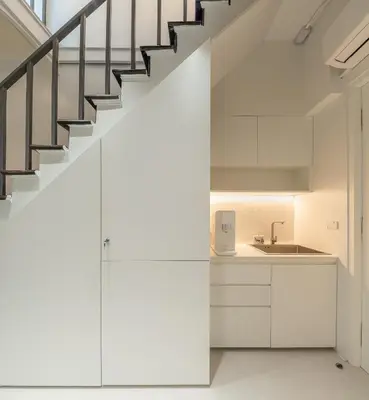 a kitchen with white cabinets and a staircase at Bedd Hostel in Bangkok