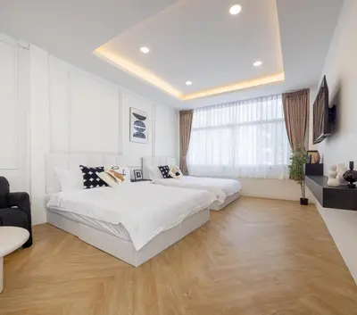 two beds in a bedroom with white walls and wood floors at Luxe apartments in Pratunam