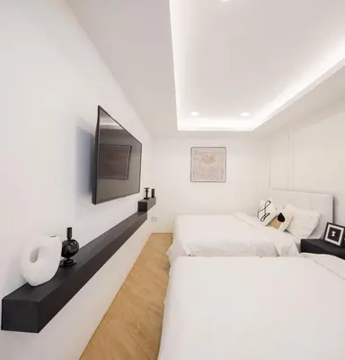 a white bedroom with two beds and a tv at Luxe apartments in Pratunam