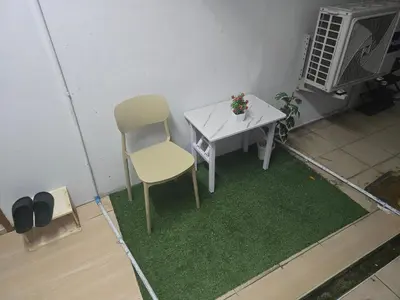 a small white table and a chair on a green rug at 103 Lovely AC apartment with private kitchen in Bangkok