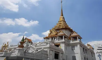 a white building with a golden roof on top at xx GO INN MRT Hua Lamphong - วัดไตรมิตร in Samphanthawong