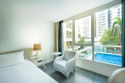 a bedroom with a bed and a chair and a window at Le Tada Parkview Hotel in Bangkok