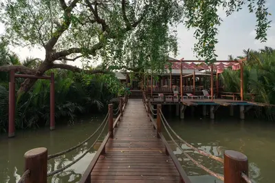 a wooden bridge over a body of water with a restaurant at Baan Krai Nao The Riverfront in Bang Chak