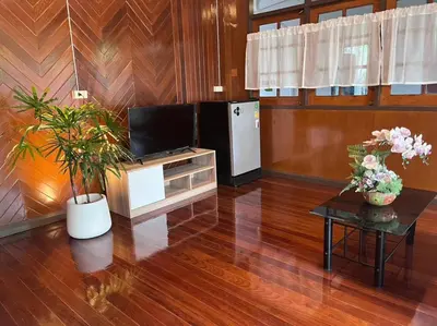 a living room with a television and a table with flowers at Chan Klong No8 Homestay - บ้านชานคลองหมายเลข8 in Sathani Wat Sing