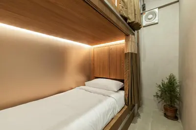 a small room with a bed with a wooden headboard at The District Hostel Ekkamai in Sathani Khlong Tan