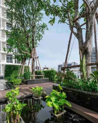 a garden with trees and a pond in front of a building at Sky Luxury Near BTS Ekkamai pool gym Netflix in Khlong Toei