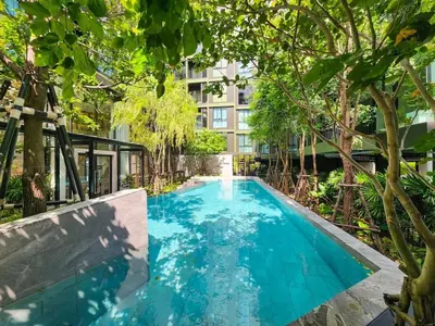 a swimming pool with trees and a building at Quiet apartment with pool close to MRT station in Bangna