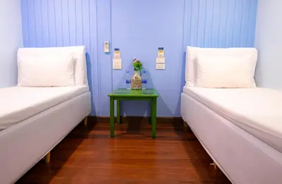 two beds in a room with a green table between them at Check-in My Hostel in Bangkok