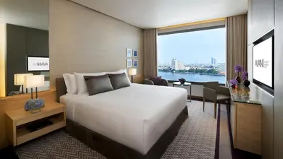 a hotel room with a bed and a desk and a window at Avani Plus Riverside Bangkok Hotel in Bangkok