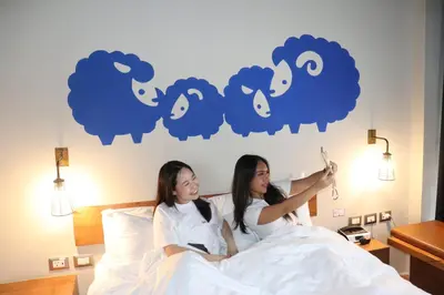 two girls laying in bed in front of a mural of sheep at Kokotel Bangkok Surawong in Bangkok