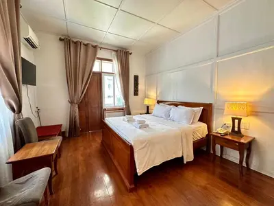 a bedroom with a bed and a chair and a window at Dinsomon Hotel in Bangkok