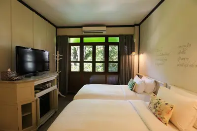two beds in a room with a tv and a window at The Raweekanlaya Bangkok Wellness Cuisine Resort in Bangkok
