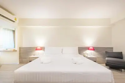 a bedroom with a large white bed and a chair at Le Tada Residence in Bangkok