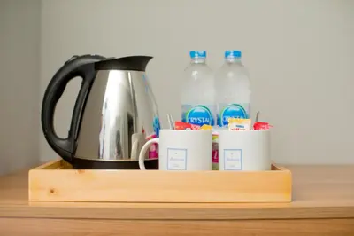 a tea kettle and cups on a wooden shelf with water bottles at The Bedroom Ladprao 101 Bangkok - SHA in Bangkok