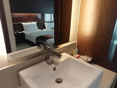 a bathroom with a sink and a mirror and a bed at Collection O The Bangkok Airport Link Suite in Bangkok