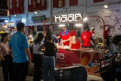 a group of people standing around a food stand at Banthat Thong Hostel in Bangkok