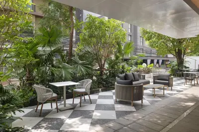 a patio with tables and chairs and trees at PARKROYAL Suites Bangkok in Bangkok