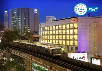 a train on a track in a city with a building at Grand 5 Hotel & Plaza Sukhumvit Bangkok in Bangkok