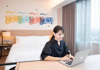 a woman sitting at a desk with a laptop in a hotel room at Modena by Fraser Bangkok in Bangkok