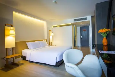 a hotel room with a white bed and a chair at Trinity Silom Hotel in Bangkok