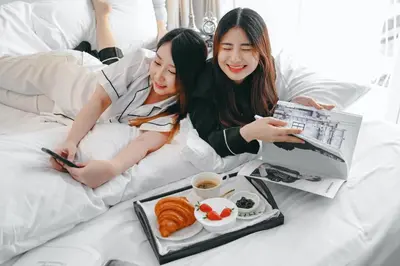 two women laying in bed with a tray of food at Noursabah Boutique Bed Bangkok in Bangkok