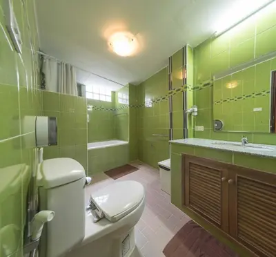a green bathroom with a toilet and a sink at Augusta in Bangkok