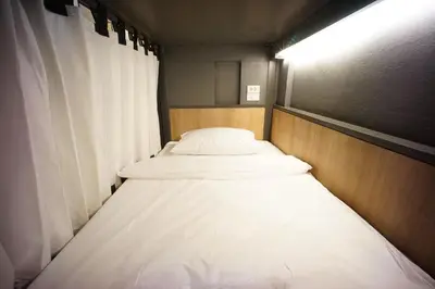two beds in a small room with white sheets at BRB Hostel Bangkok Silom in Bangkok