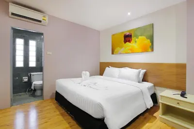 a bedroom with a large white bed and a bathroom at Pula Silom in Bangkok