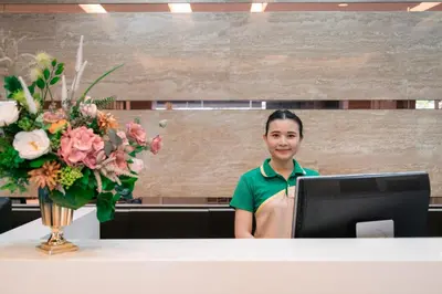 a woman standing behind a desk with a computer and a vase of flowers at At 115 Hotel By Rompo in Bangkok