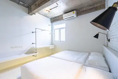 a white bedroom with a bed and a lamp at Siam Plug In Hostel in Bangkok