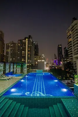 a large swimming pool with a city skyline at night at Hope Land Hotel Sukhumvit 8 in Bangkok