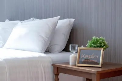 a bed with white pillows and a table with a wine glass at Kepler Residence Bangkok in Bangkok