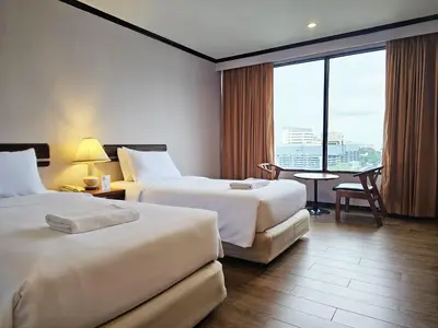 a hotel room with two beds and a table and a window at Alexander Hotel in Bangkok