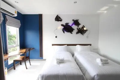two beds in a room with blue walls and a desk at Anna-Nava Pakkret Hotel in Nonthaburi