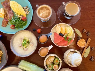 a wooden table with plates of food and cups of coffee at Bliston Suwan Park View in Bangkok