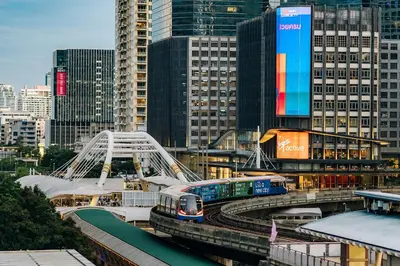 a train on tracks in a city with buildings at Sora Hotel Silom in Bangkok