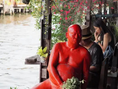a red statue of a man sitting next to a river at 28 Place in Bangkok