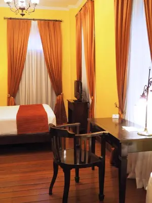 a bedroom with a desk and a bed with orange curtains at Praya Palazzo in Bangkok