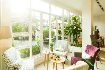 a living room with chairs and tables and windows at Hotel De Bangkok in Bangkok