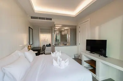 a white bedroom with a white bed and a flat screen tv at Siam Tharadol in Bangkok