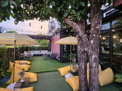 a patio with tables and umbrellas and a tree at Wayha Hostel Don Mueang Airport in Bangkok