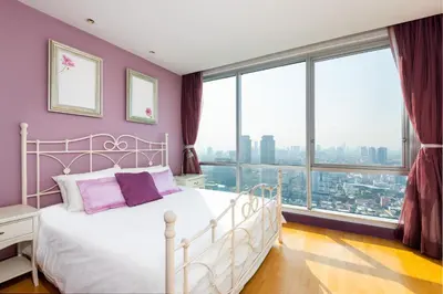 a bedroom with a white bed with purple walls and large windows at Sky Villas Apartments in Bangkok