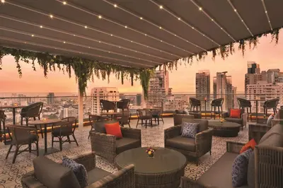 a rooftop patio with tables and chairs and a city skyline at Hyatt Place Bangkok Sukhumvit 24 in Bangkok
